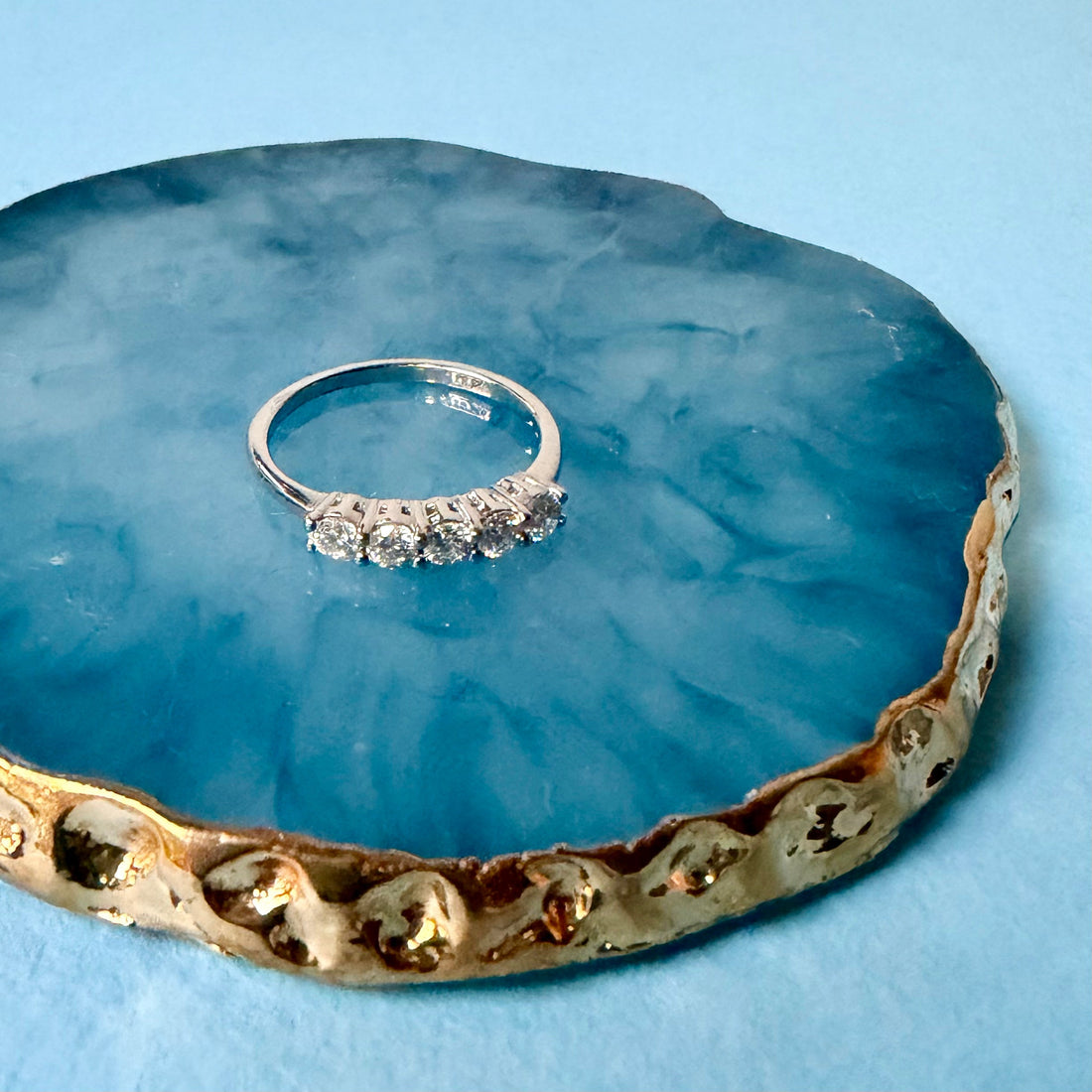 Moissanite eternity band sitting on a blue marbled tray with gold edges